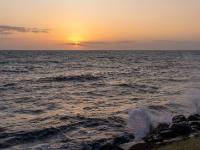 Sonnenuntergang hinter Wolkenschicht und gischtende Wellen am Ufer - Rønne